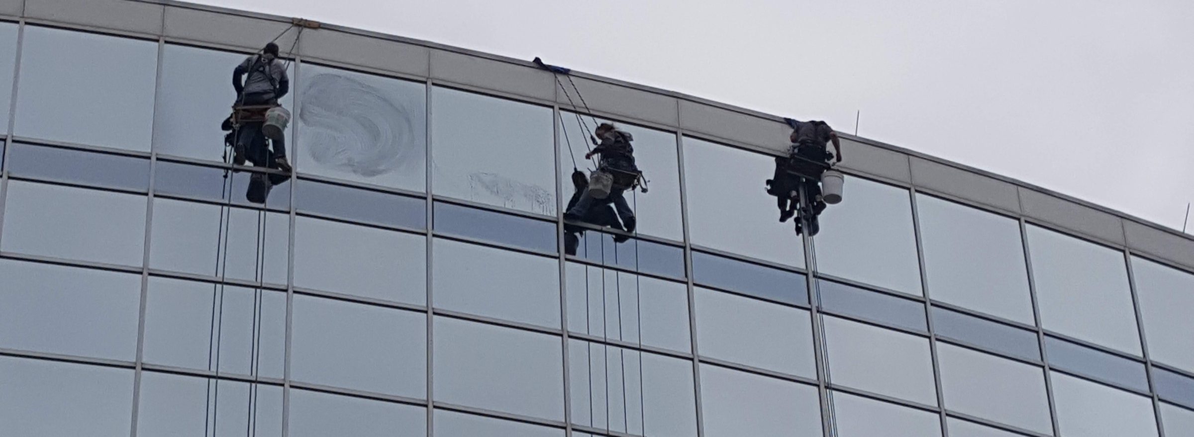 Three Miracle technicians on rope access doing high-rise window cleaning on a curved glass curtain wall in Little Rock Arkansas