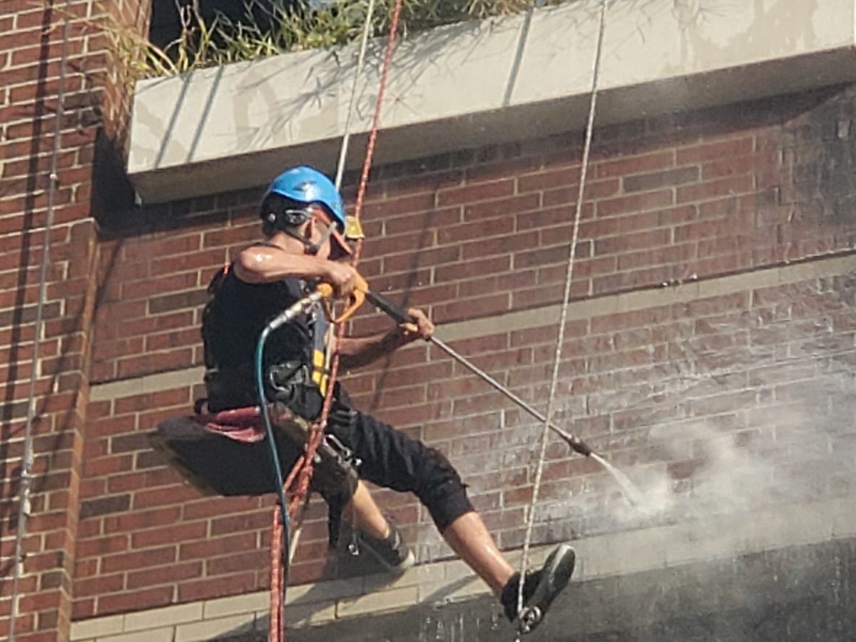 Miracle technician in a helmet and harness pressure washing a brick facade from rope access lines in Central Arkansas